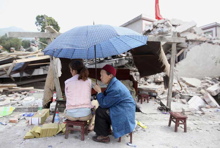 En esta foto difundida por la agencia de noticias Xinhua de China, los residentes se sientan al lado de las ruinas de las casas destruidas por el terremoto de Longmen Township.